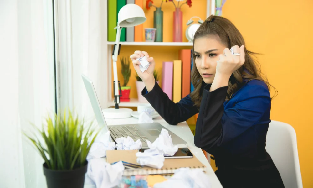 A woman in a blue blazer looks frustrated at her laptop