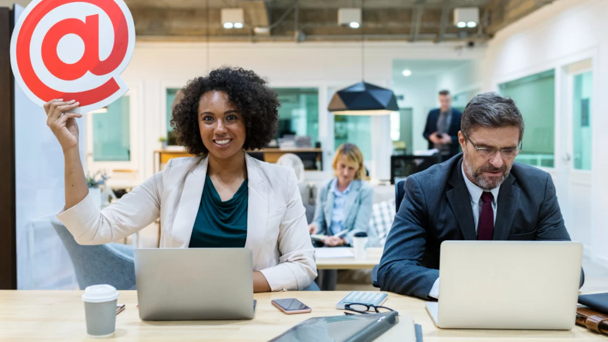 woman in a light blazer smiles and holds an @ symbol